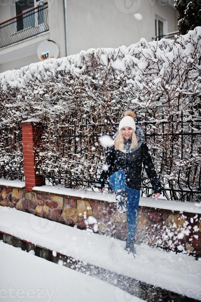 Blondes Mädchen, das sich am Wintertag mit Schnee amüsiert. foto