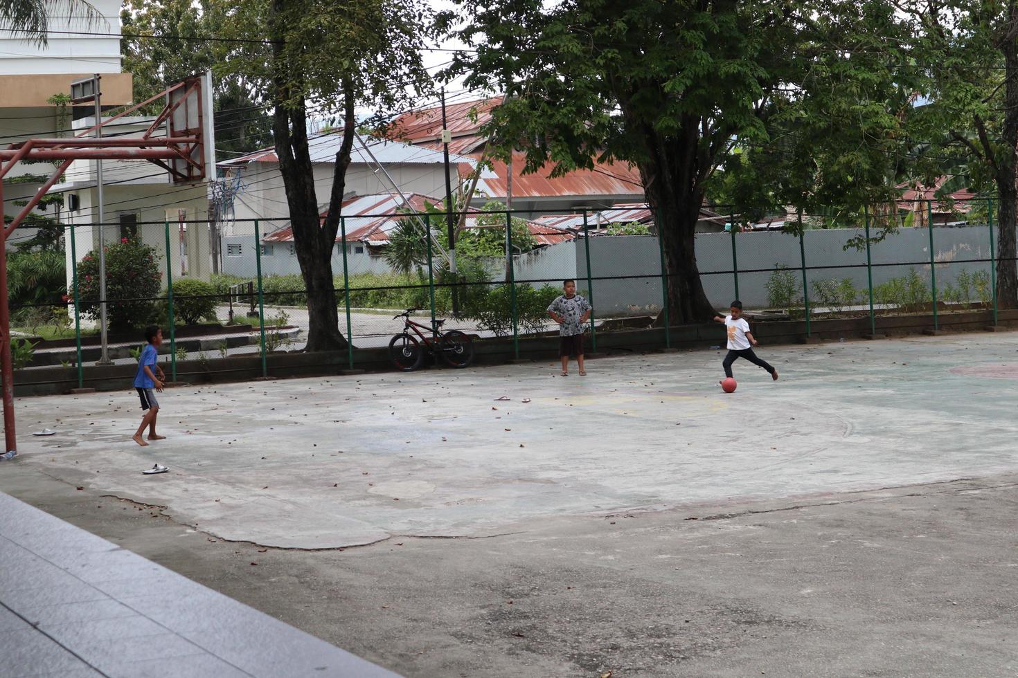 gorontalo-indonesien, juni 2022 - kinder üben tagsüber fußball auf einem basketballplatz foto