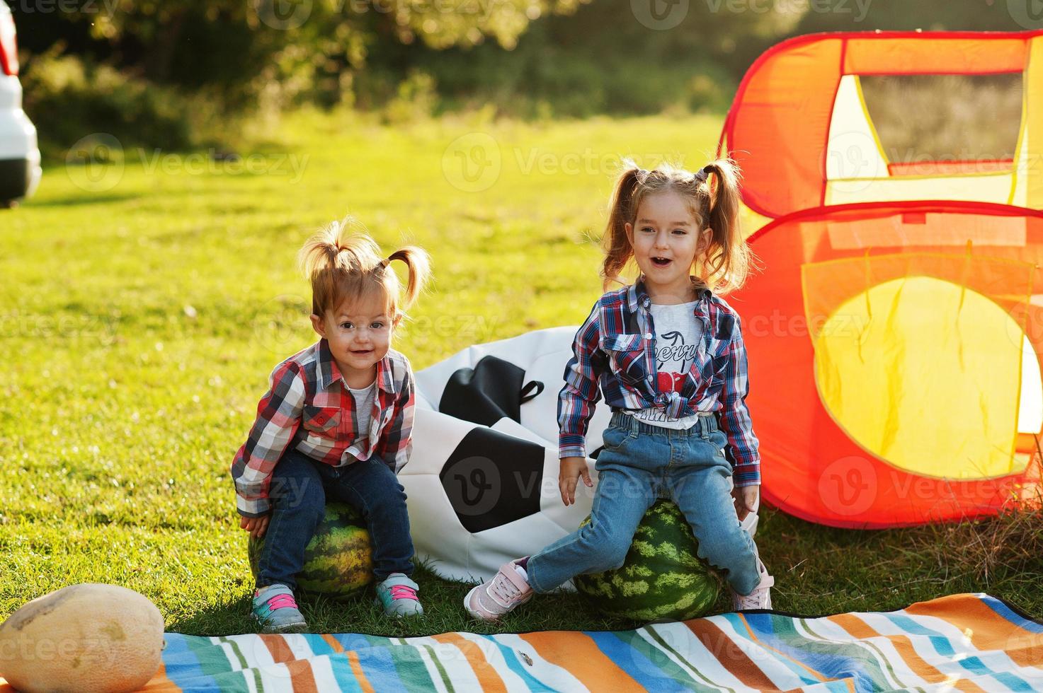 Zwei kleine süße Schwestermädchen im Freien beim Picknick, tragen ein kariertes Hemd. auf Wassermelone sitzen. foto