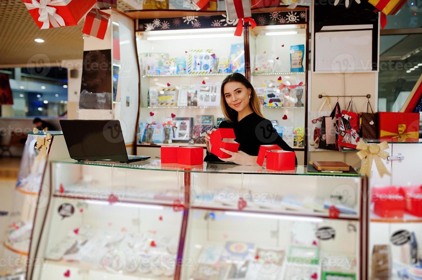 Porträt einer jungen kaukasischen Verkäuferin mit roten Geschenkboxen. kleines Geschäft mit Süßigkeiten-Souvenir-Shop. foto