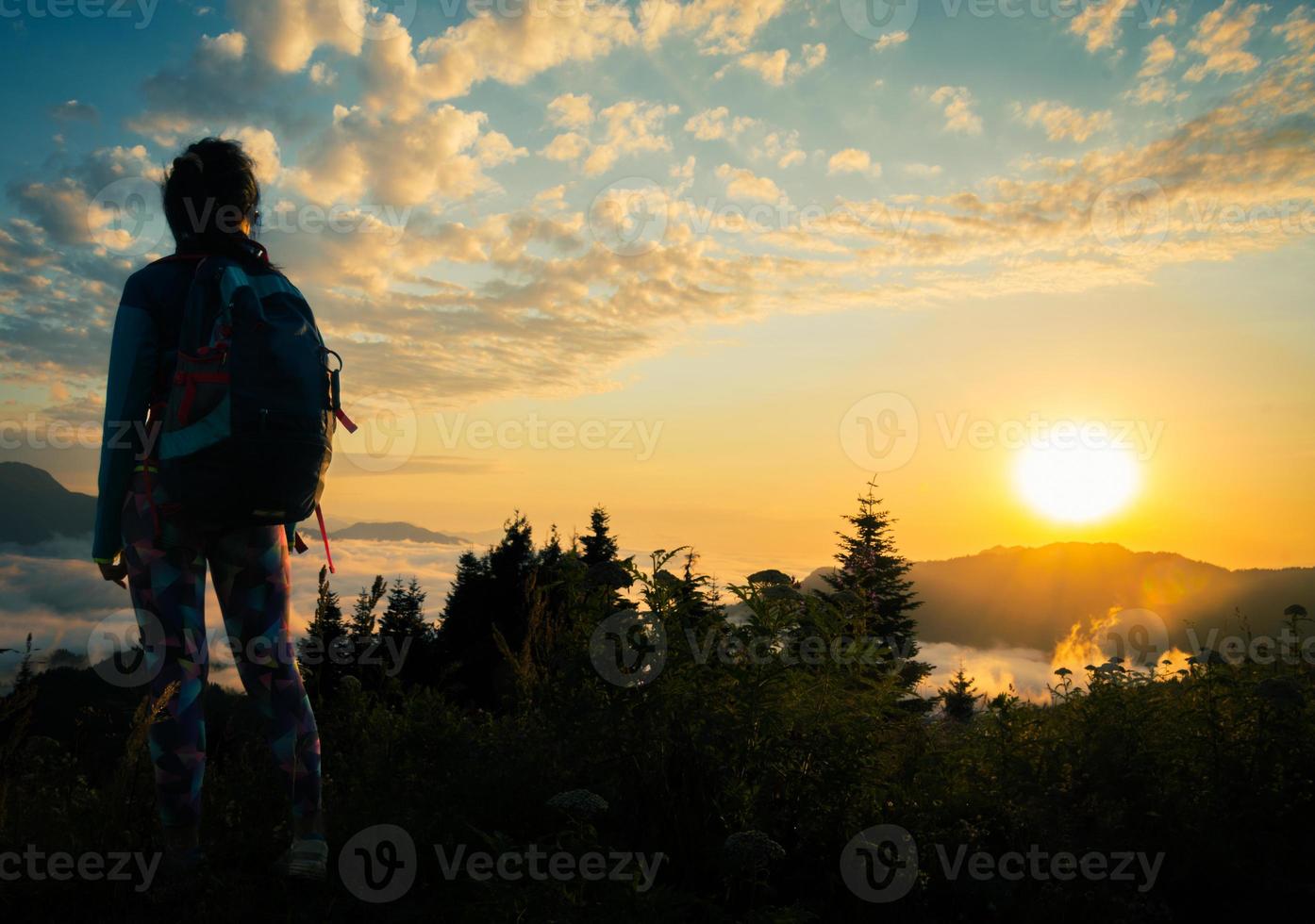 Junge, fitte, glückliche Frau steht auf Aussichtspunkt, nachdem sie die Spitze in den Bergen erreicht hat. sorglose Touristenfrau, die die Sonne betrachtet und die Landschaft genießt. Reisender auf dem Gipfel des Berges in den Strahlen des Sonnenuntergangs foto