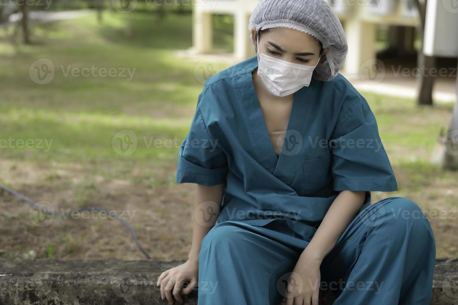 müde depressive asiatische krankenschwester trägt gesichtsmaske blaue uniform sitzt auf dem krankenhausboden, junge ärztin gestresst von harter arbeit foto