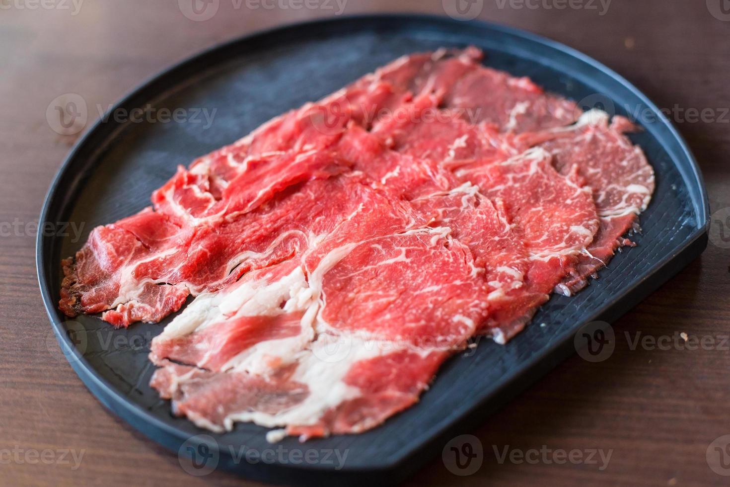 frisches Rindfleisch wurde roh in Scheiben geschnitten für das Restaurant Sukiyaki und Shabu oder Yakiniku serviert, das auf einen schwarzen Teller gestellt wurde. foto