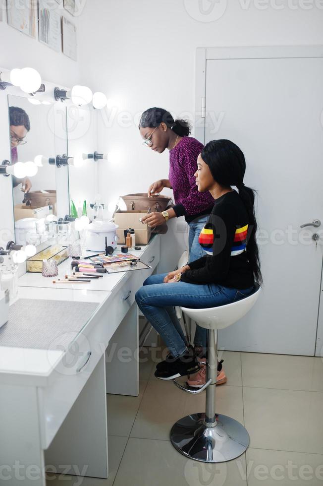 Afroamerikanerin beim Schminken durch Make-up-Künstlerin im Schönheitssalon. foto