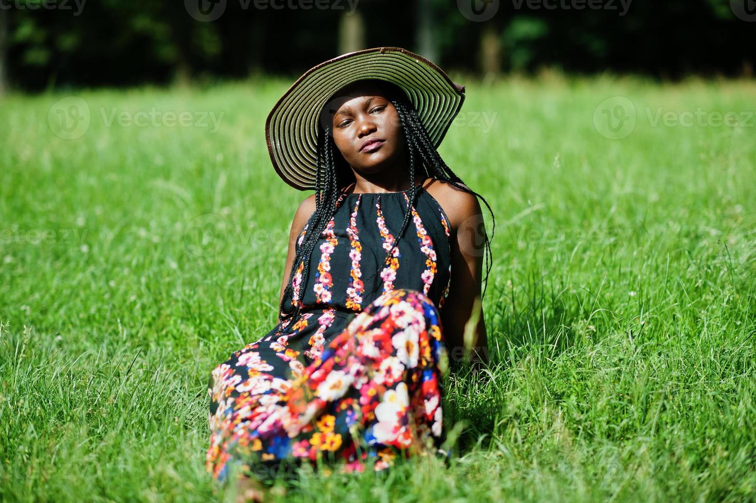 Porträt einer wunderschönen afroamerikanischen Frau der 20er Jahre mit Sommerhut, die auf grünem Gras im Park sitzt. foto