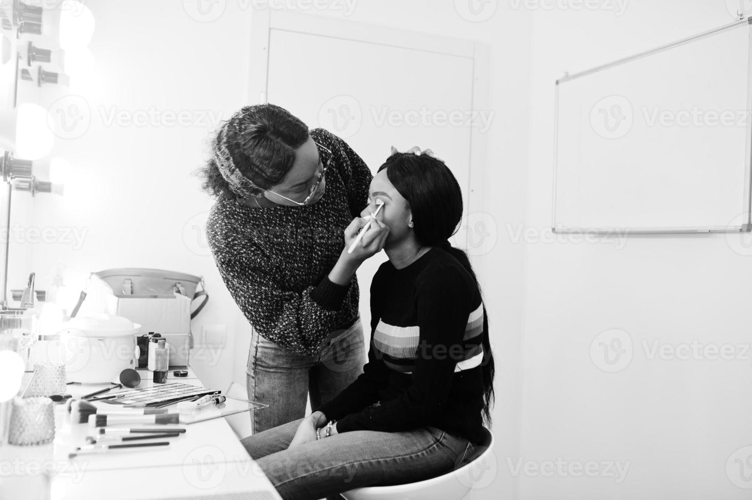 Afroamerikanerin beim Schminken durch Make-up-Künstlerin im Schönheitssalon. foto