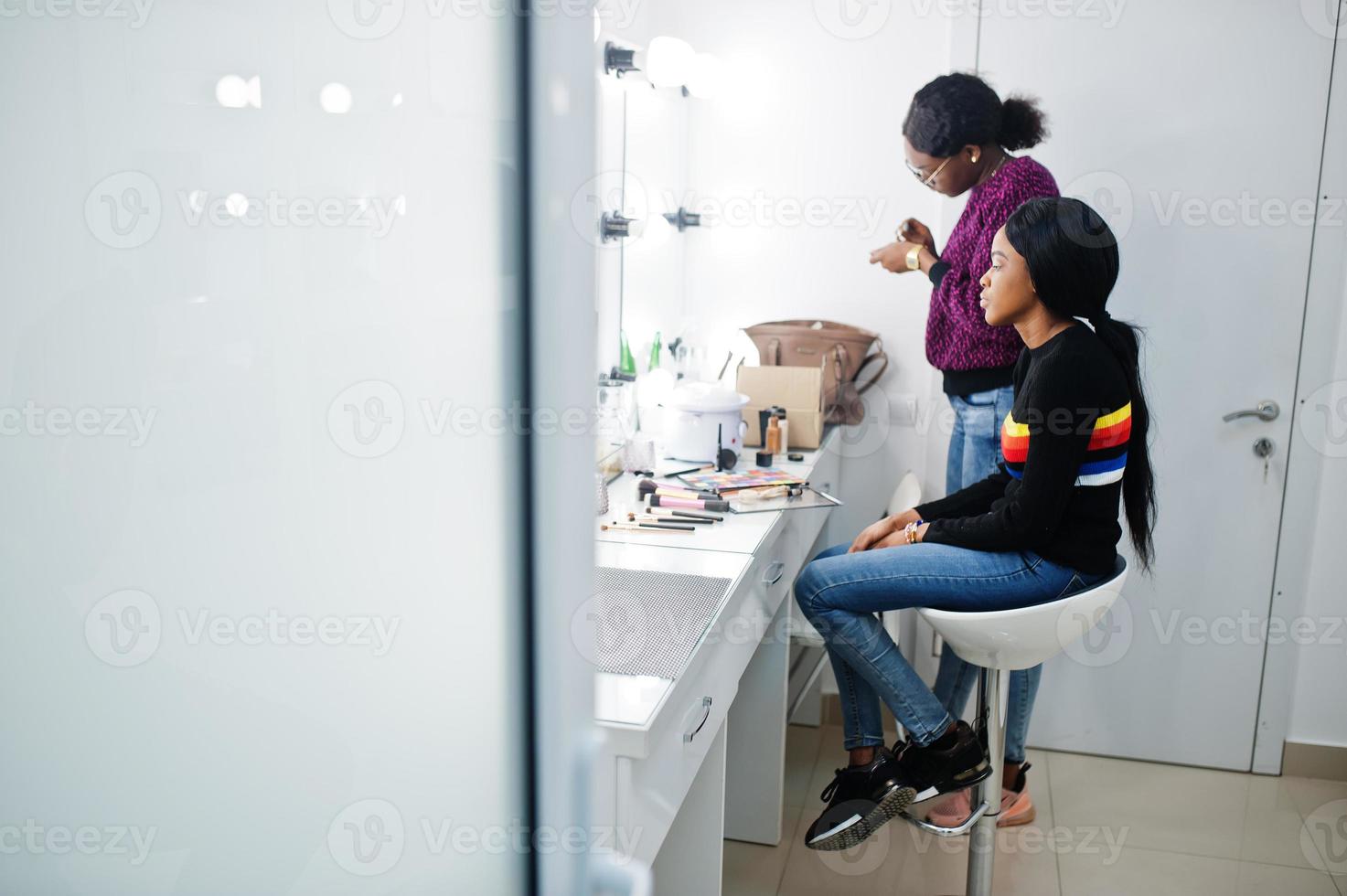 Afroamerikanerin beim Schminken durch Make-up-Künstlerin im Schönheitssalon. foto