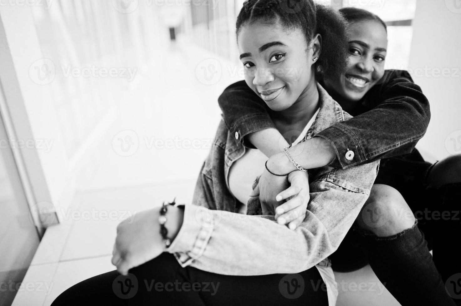 zwei afrikanische freundinnen in jeansjacke sitzen zusammen drinnen. foto