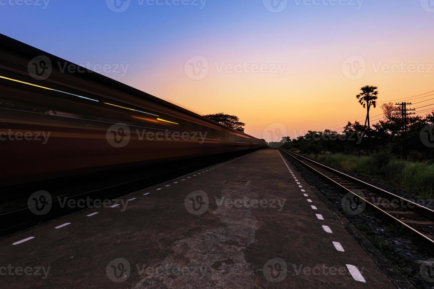 Zug fährt im Sonnenuntergang durch den Bahnhof foto
