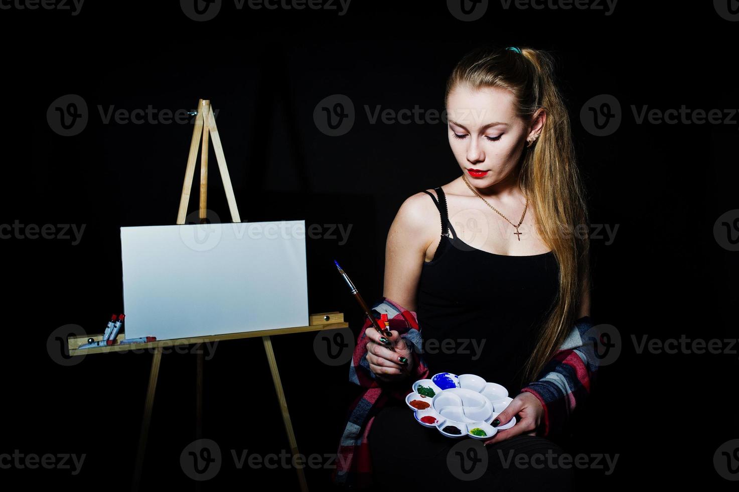 schöne Künstlerin Malerin mit Pinsel und Ölleinwand posiert im Studio isoliert auf schwarz. foto