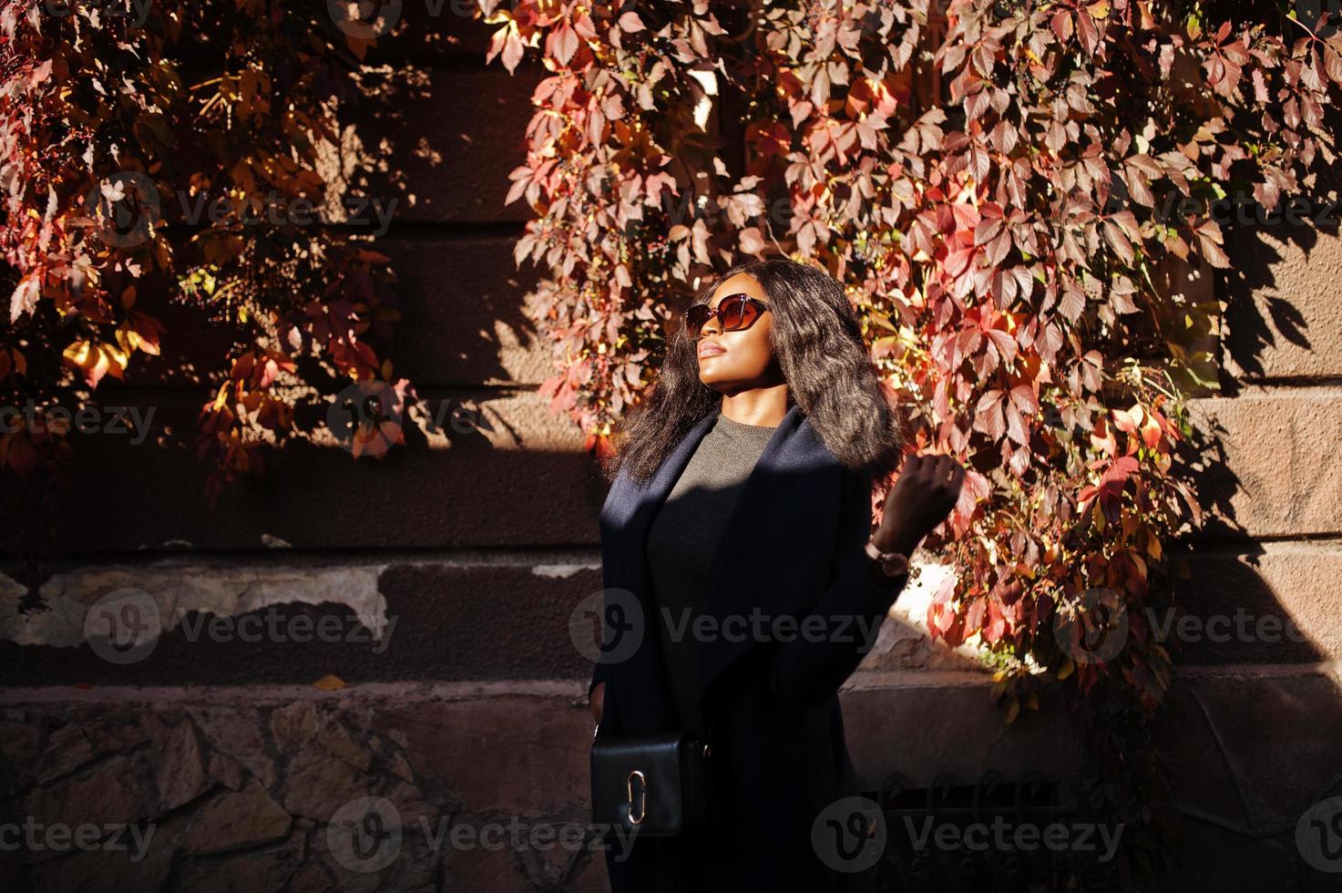 stilvolles afroamerikanisches mädchen in blauem mantel und sonnenbrille posierte am sonnigen herbsttag. afrikanische vorbildliche frau. foto