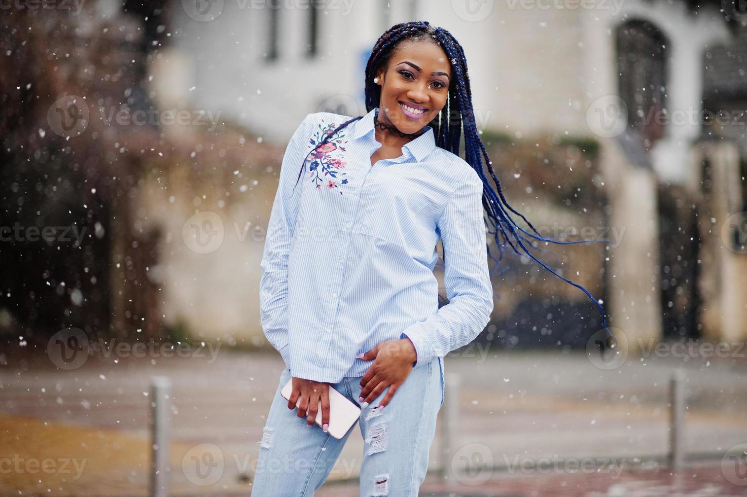 stilvolles afrikanisch-amerikanisches Mädchen mit Dreads, das Handy zur Hand hält, Schneewetter im Freien. foto