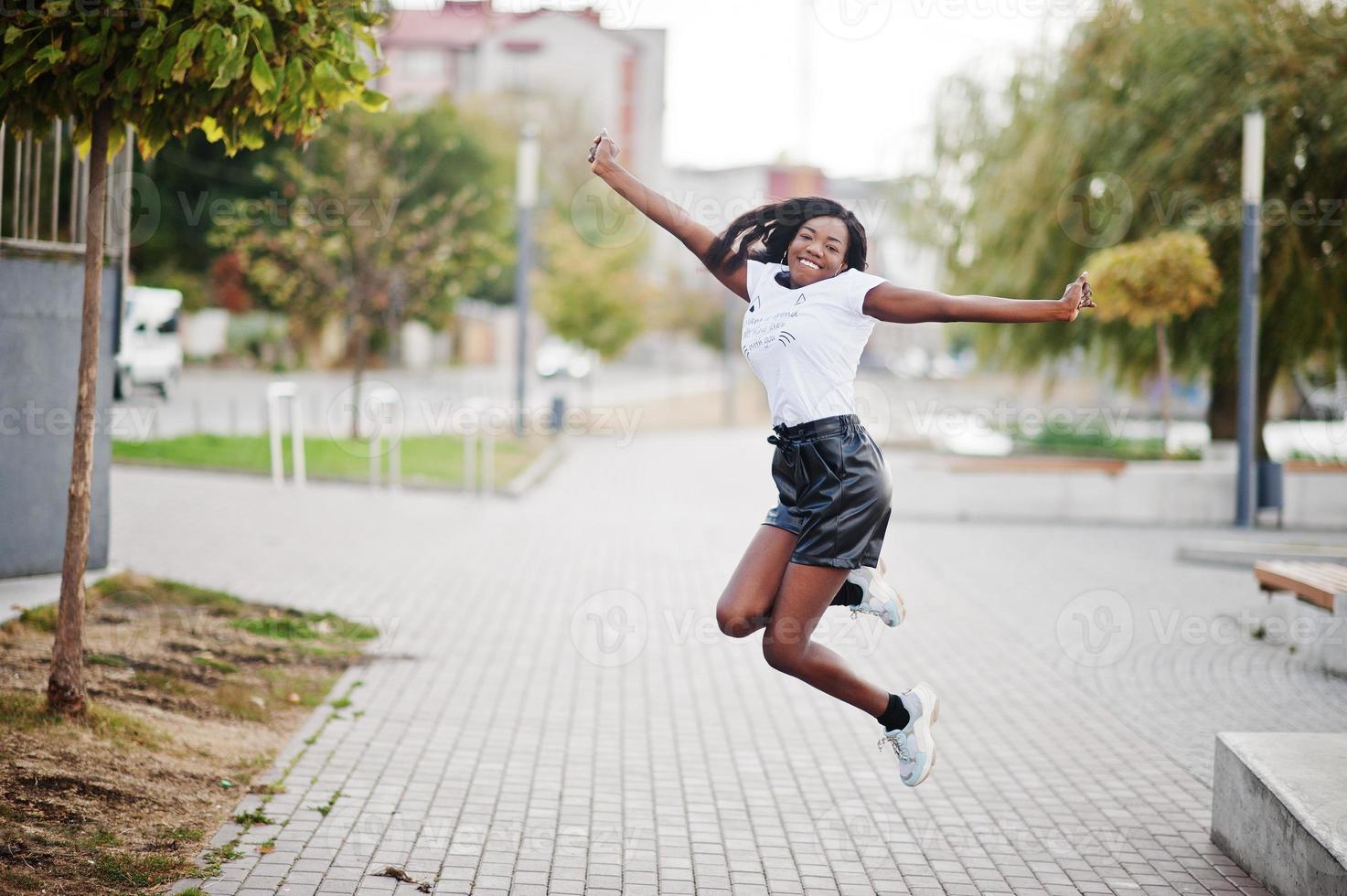 afroamerikanisches, dunkelhäutiges, schlankes Model posiert in schwarzen Ledershorts und weißem T-Shirt. sie springt in die Luft. foto