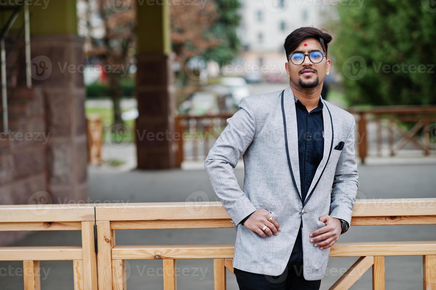 stilvoller indischer mann mit bindi auf stirn und brille, trägt einen grauen anzug, der im freien posiert. foto