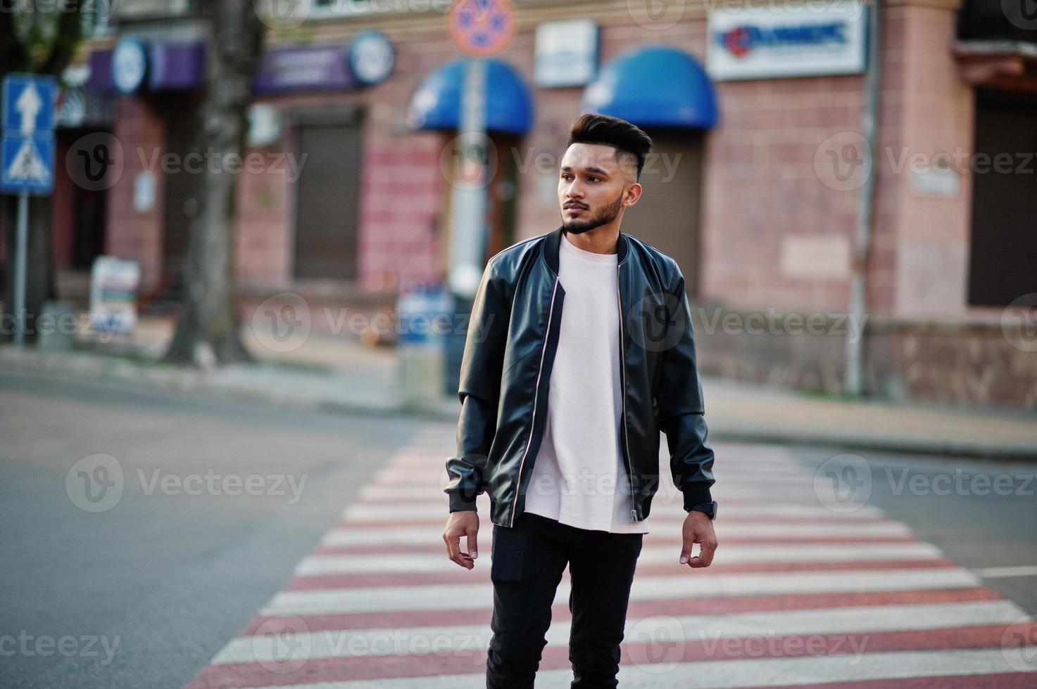 stilvoller indischer bartmann in schwarzer lederjacke, der auf zebrastreifen geht. Indien-Model posierte im Freien auf den Straßen der Stadt. foto