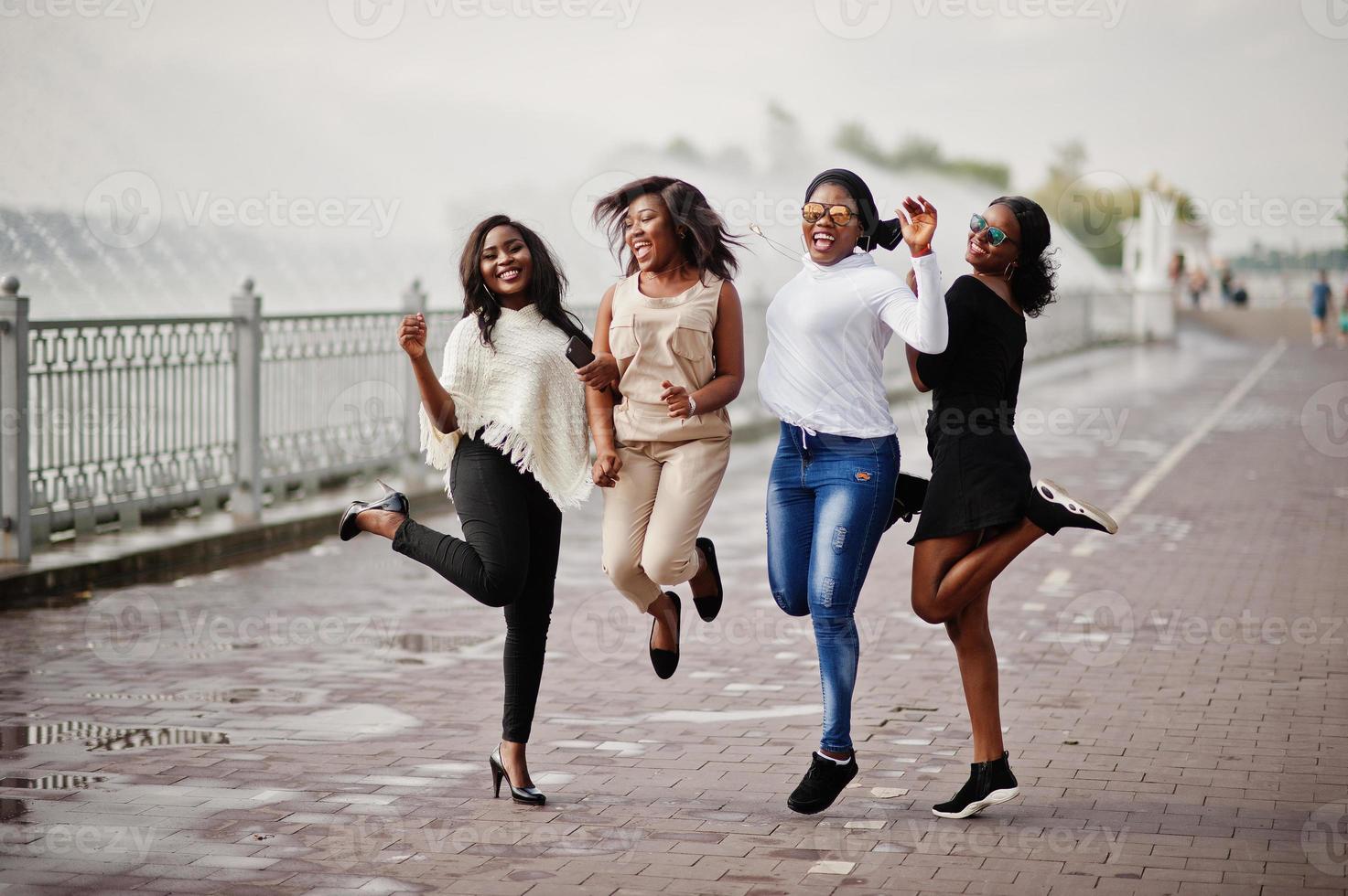 Gruppe von vier afroamerikanischen Mädchen, die Spaß haben und mit Springbrunnen gegen den See springen. foto