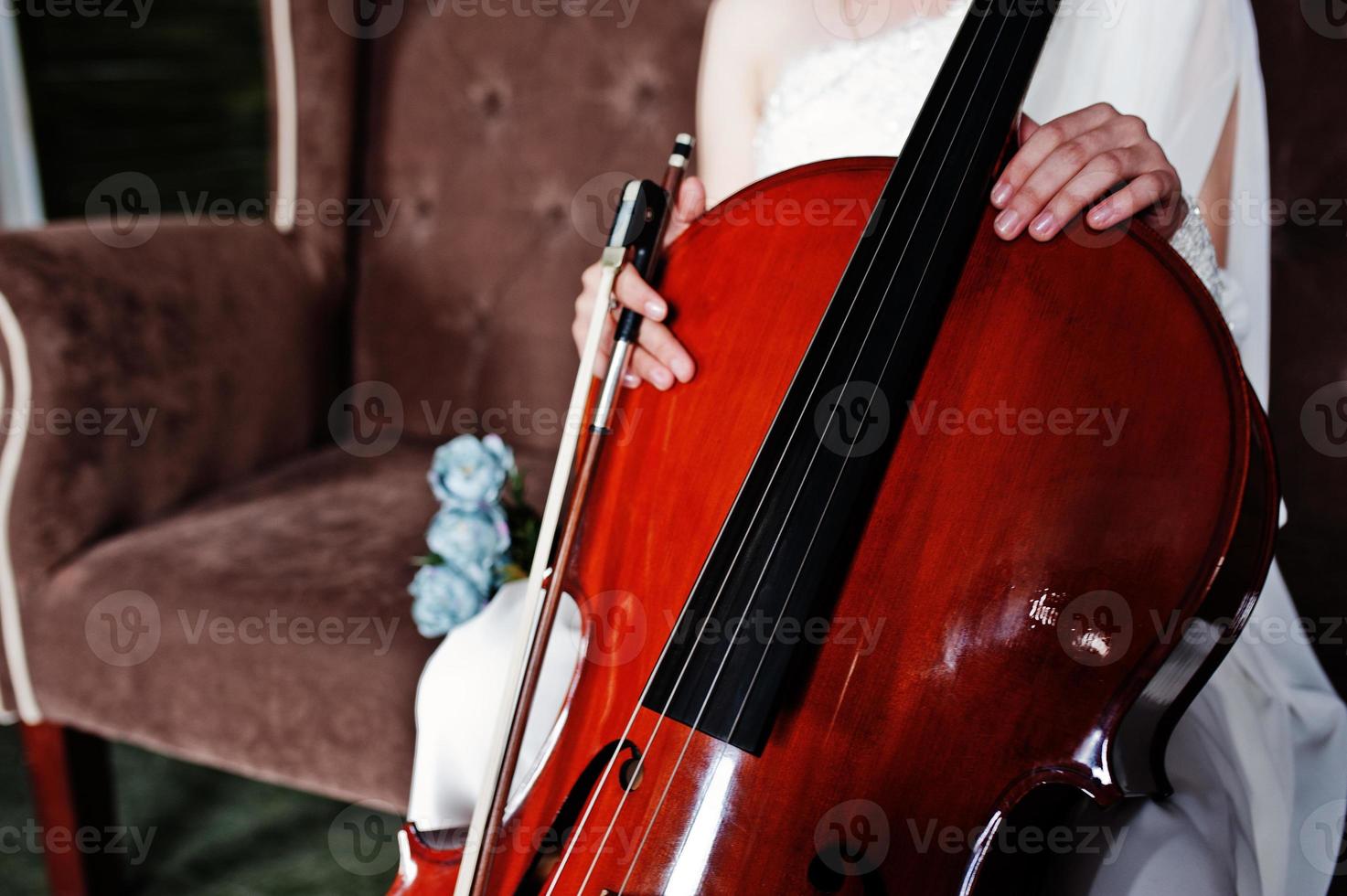 Nahaufnahme eines Gilrl-Musikers in weißem Kleid mit Kontrabass, der auf einem braunen Vintage-Sofa sitzt. foto