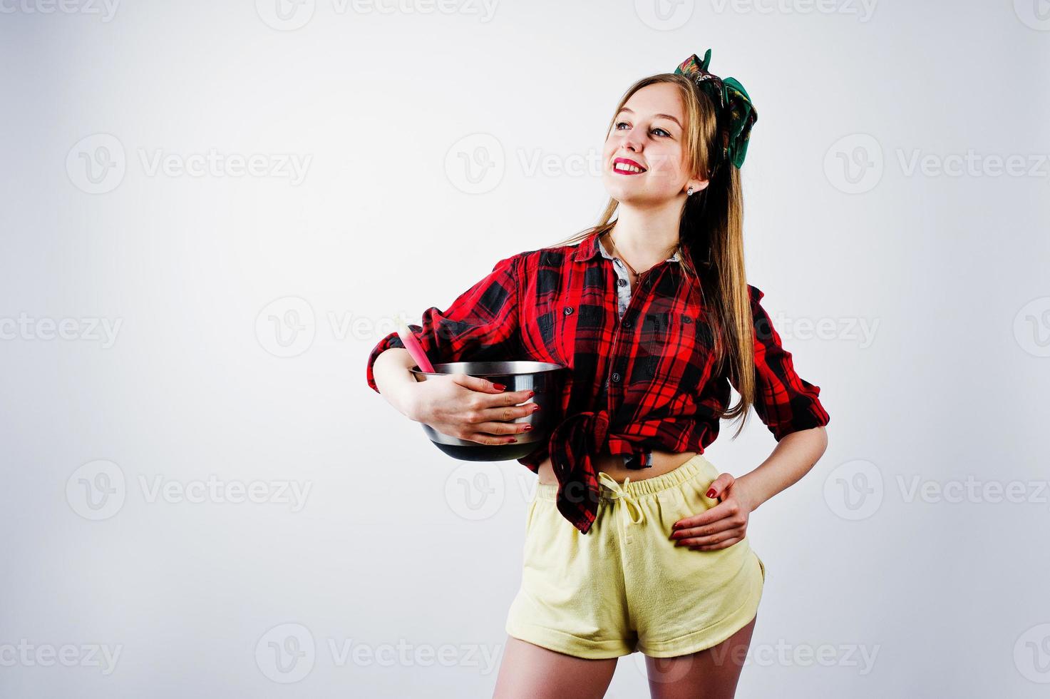 junge lustige Hausfrau in kariertem Hemd und gelben Shorts Pin-up-Stil mit Topf und Küchenlöffel isoliert auf weißem Hintergrund. foto