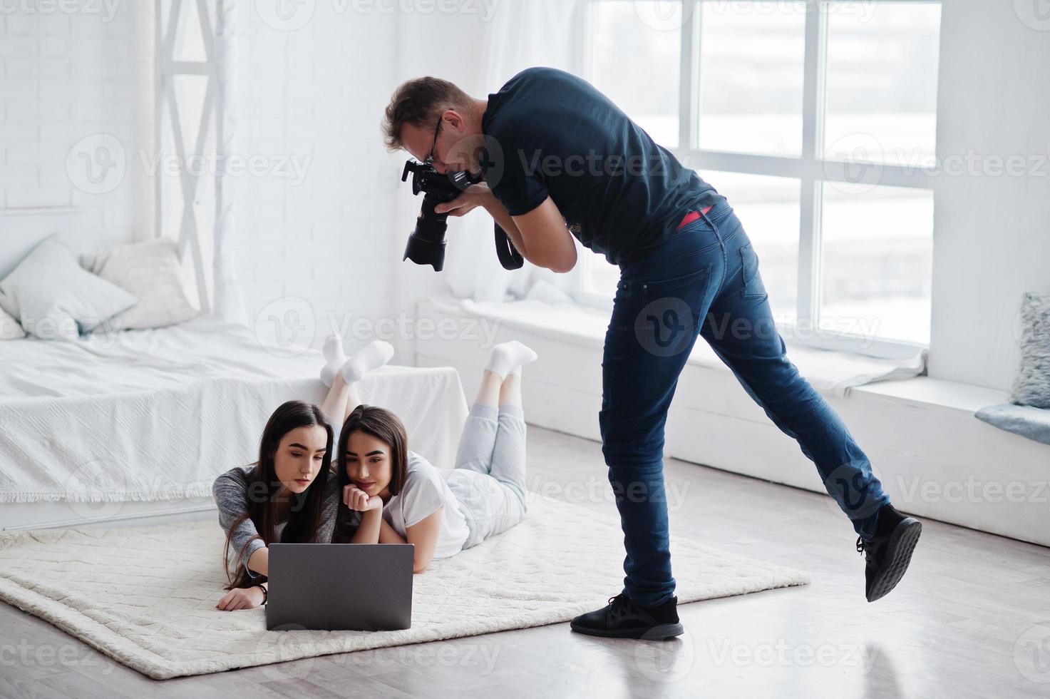 Fotograf schießt im Studio zwei Zwillingsmodelle, die auf den Laptop schauen. professioneller fotograf bei der arbeit. Meisterklasse. foto