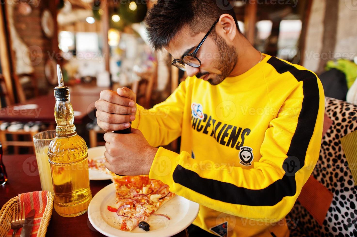 asiatischer mann, der pizza während der party in der pizzeria isst. Typ, der italienisches Essen isst und auf der Couch sitzt, Pfeffer einschenkt. foto