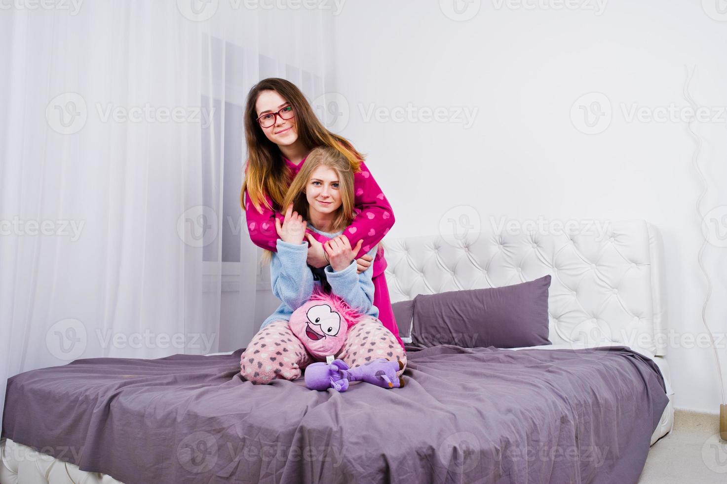 zwei befreundete mädchen im pyjama haben spaß auf dem bett im zimmer. foto