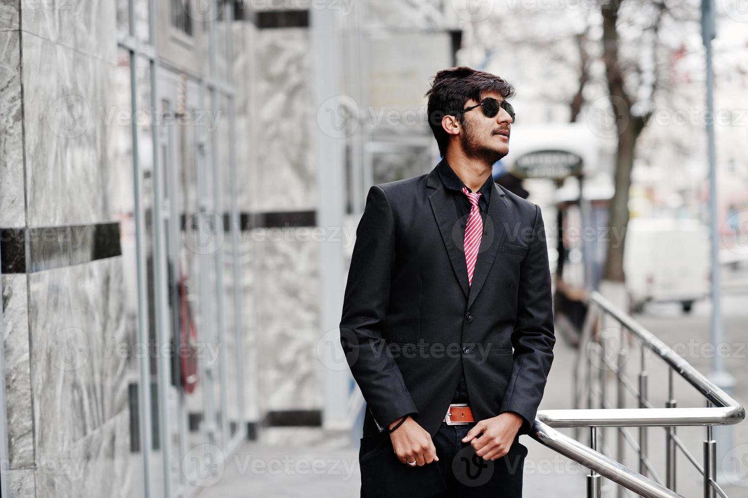 junger indischer mann auf anzug, krawatte und sonnenbrille posierte im freien. foto