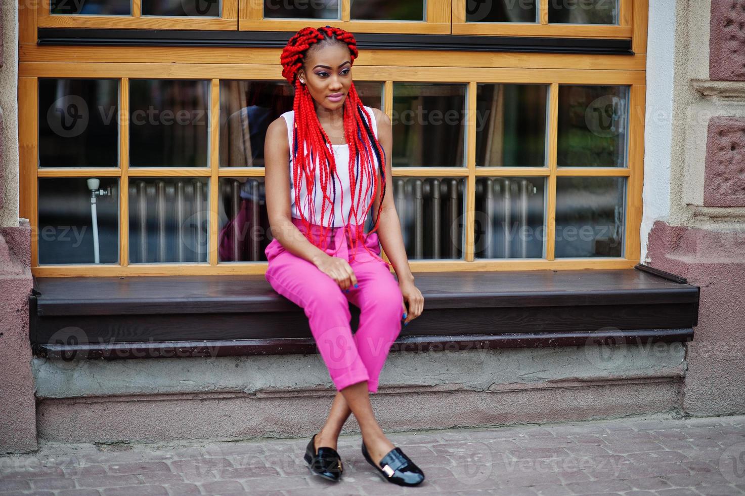 Modisches afroamerikanisches Mädchen in rosa Hosen und roten Dreads posierte im Freien. foto