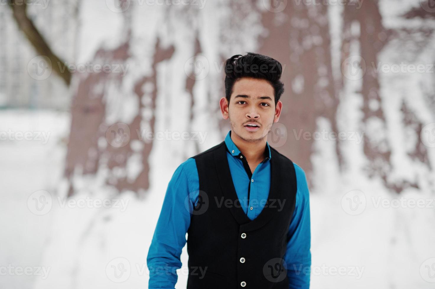 Lässiger junger indischer Mann in blauem Hemd und schwarzer Weste posierte am Wintertag. foto
