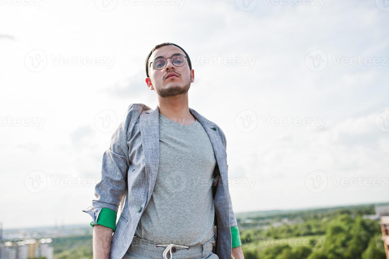 träumer stylischer machomann in grauem anzug, hut und brille posierte auf dem dach. foto