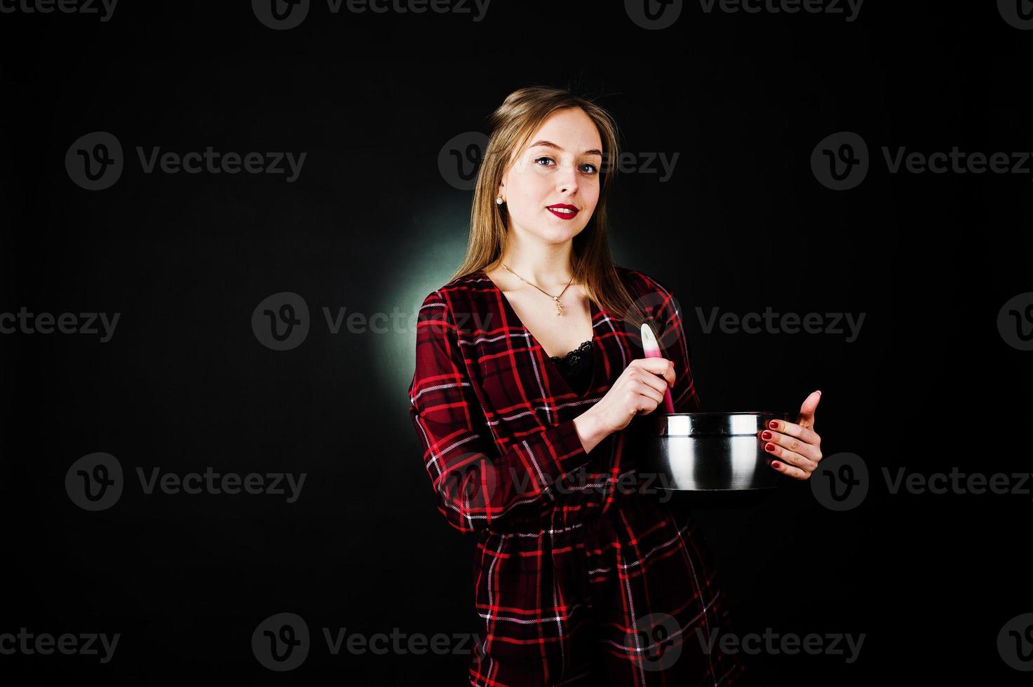 junge Hausfrau im karierten Kleid mit Topf und Kochlöffel auf schwarzem Hintergrund isoliert. foto