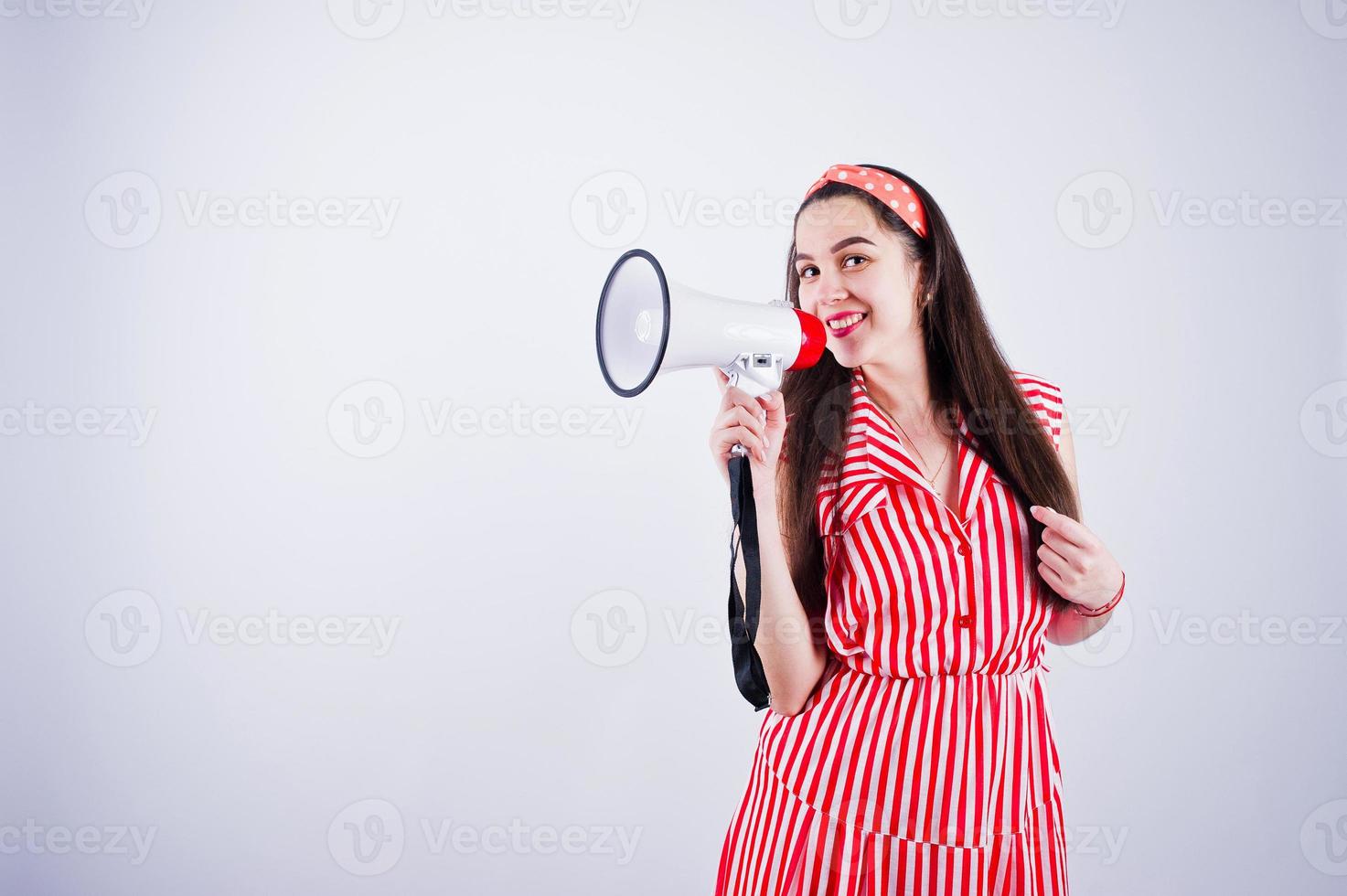 Porträt einer jungen schönen Frau in rotem Kleid, die in ein Megaphon spricht. foto