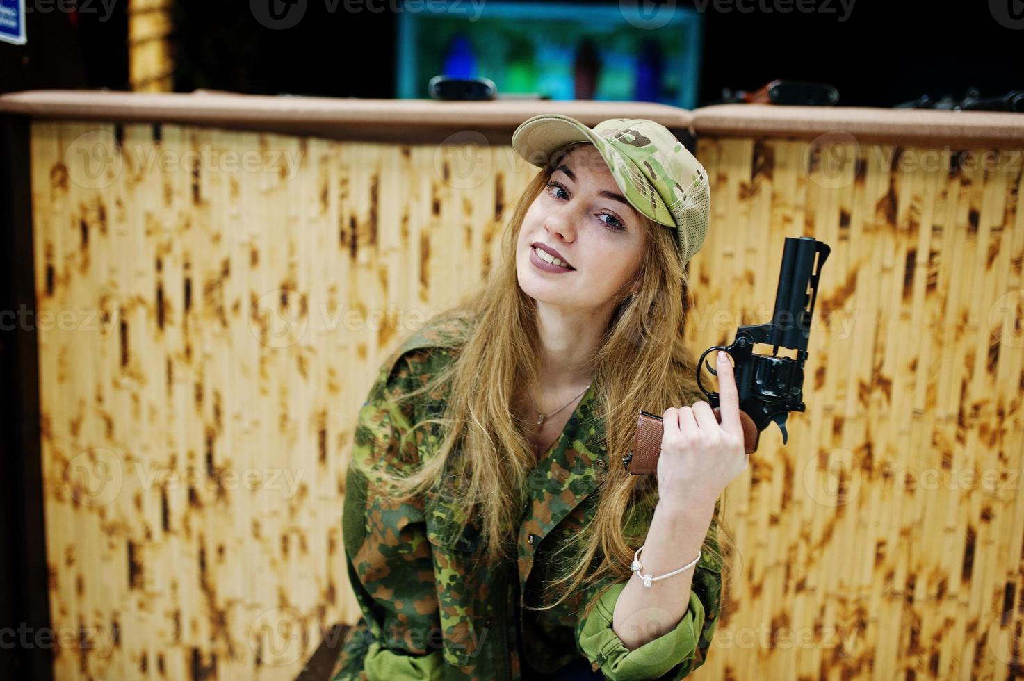 militärmädchen in tarnuniform mit revolverpistole zur hand vor armeehintergrund auf schießstand. foto