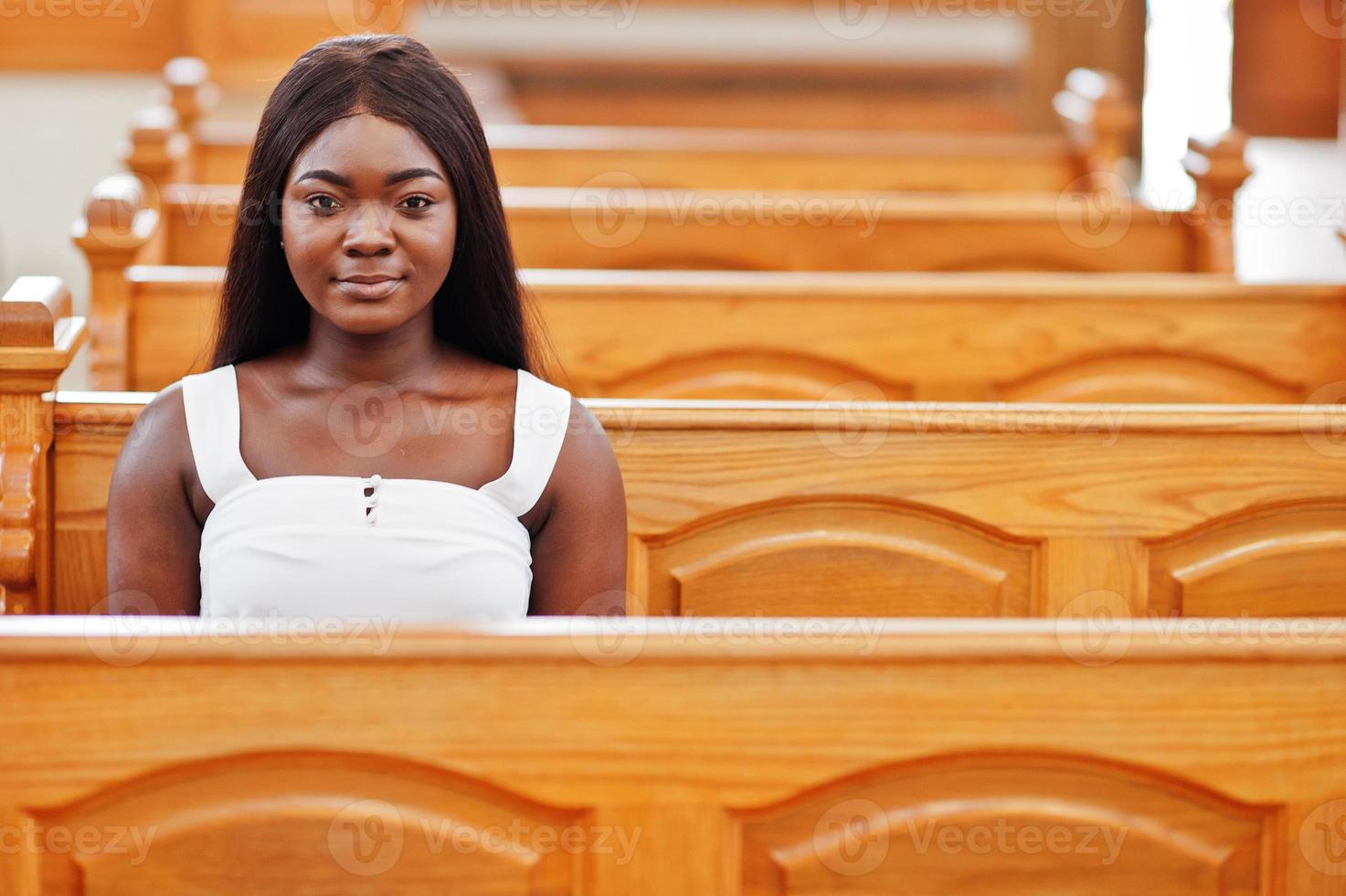 Afroamerikanerin, die in der Kirche betet. Gläubige meditieren in der Kathedrale und spirituelle Gebetszeit. Afro-Mädchen, das auf einer Bank sitzt. foto