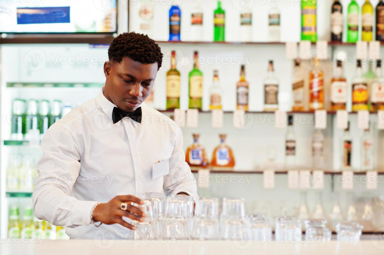 afroamerikanischer barkeeper trägt an der bar eine fliege, die eine brille putzt. foto