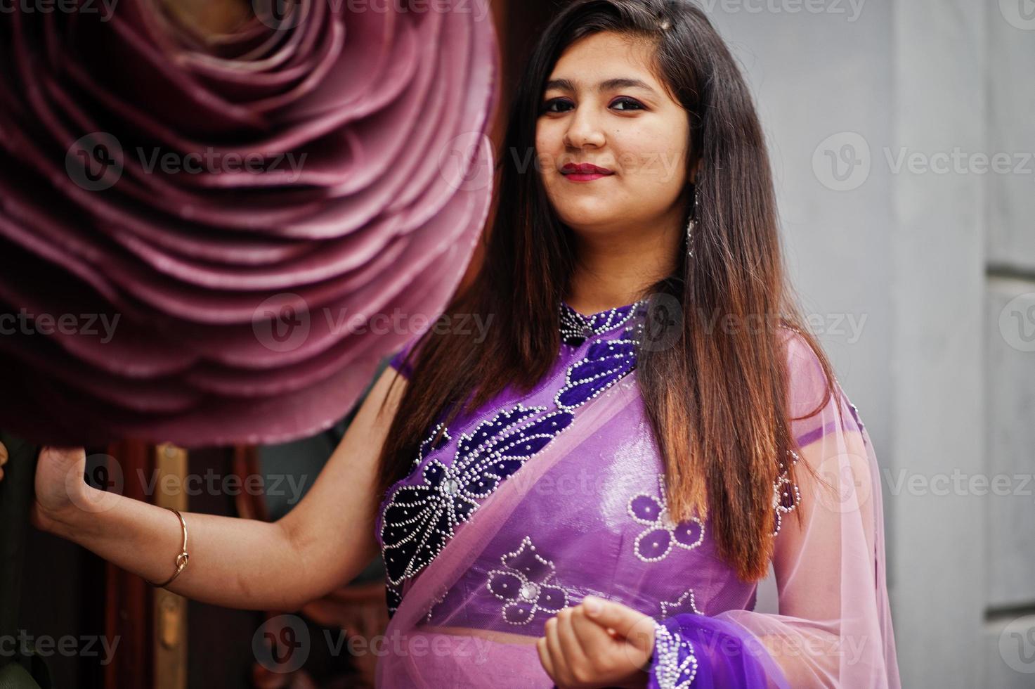 Indisches hinduistisches Mädchen im traditionellen violetten Saree posierte auf der Straße in der Nähe einer großen geschmückten Rose. foto