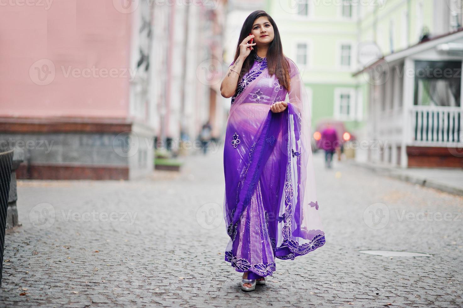 Indisches hinduistisches Mädchen im traditionellen violetten Saree posierte auf der Straße und sprach am Telefon. foto