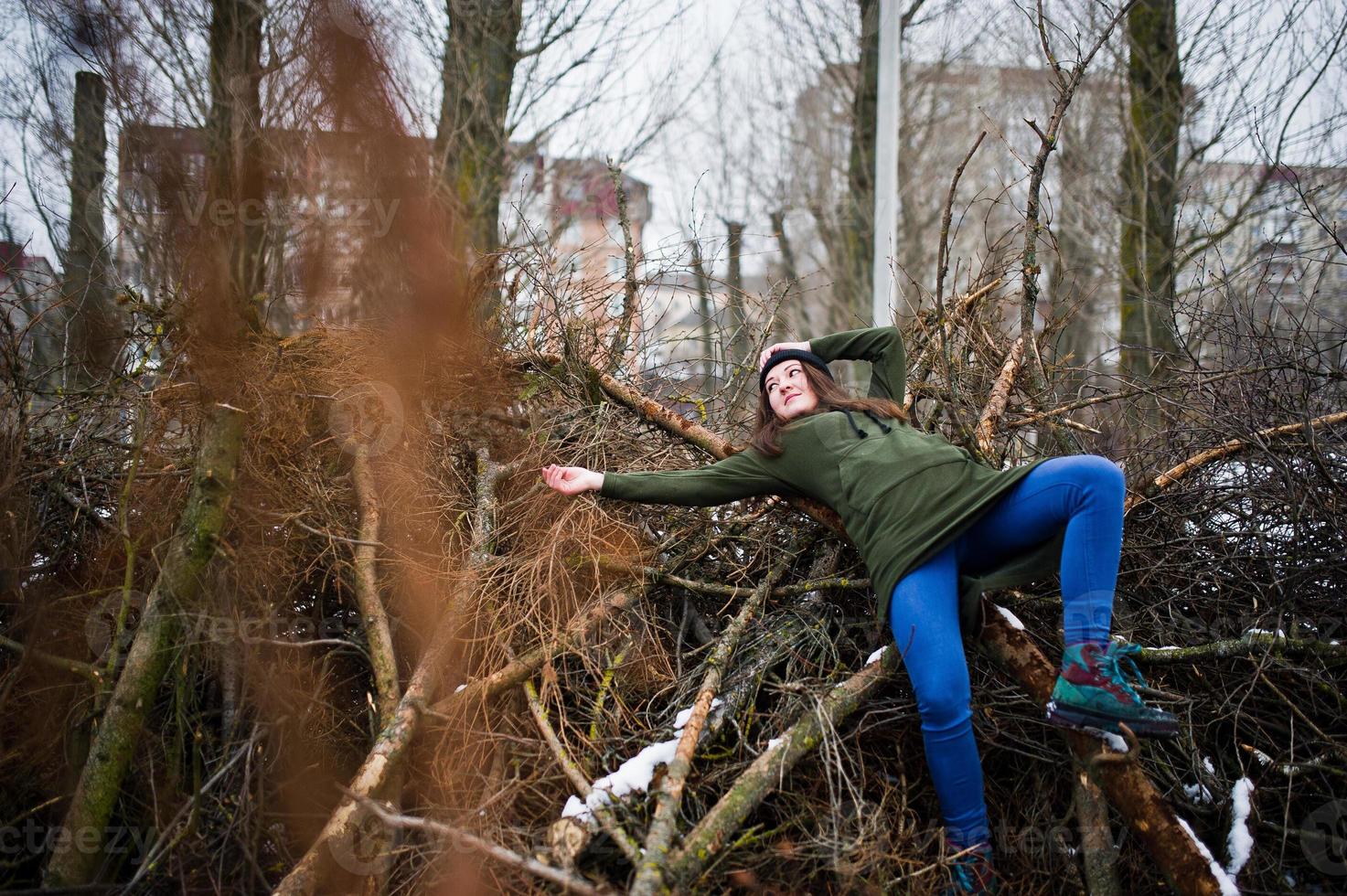 junge Mädchen tragen am Wintertag ein langes grünes Sweatshirt, Jeans und schwarze Kopfbedeckungen an Ästen der Kiefer. foto