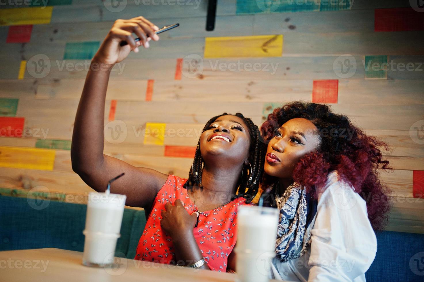 Attraktive afroamerikanische zwei Freundinnen sitzen im Café mit Latte und machen Selfie auf dem Handy. foto