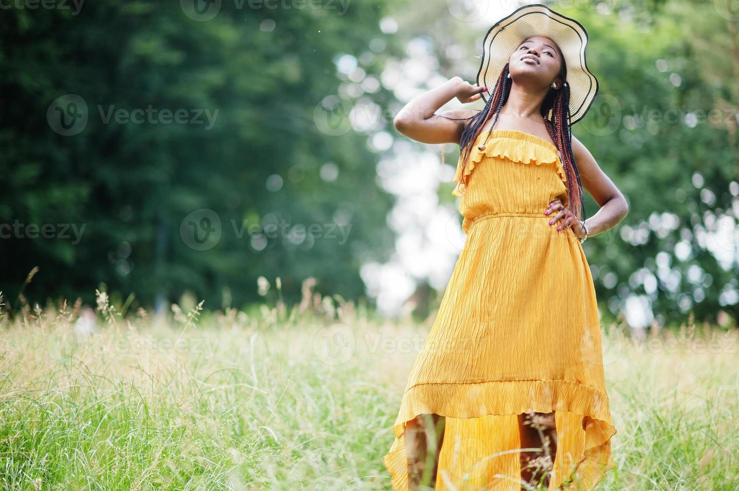 Porträt einer wunderschönen afroamerikanischen Frau der 20er Jahre in gelbem Kleid und Sommerhut, die auf grünem Gras im Park posiert. foto