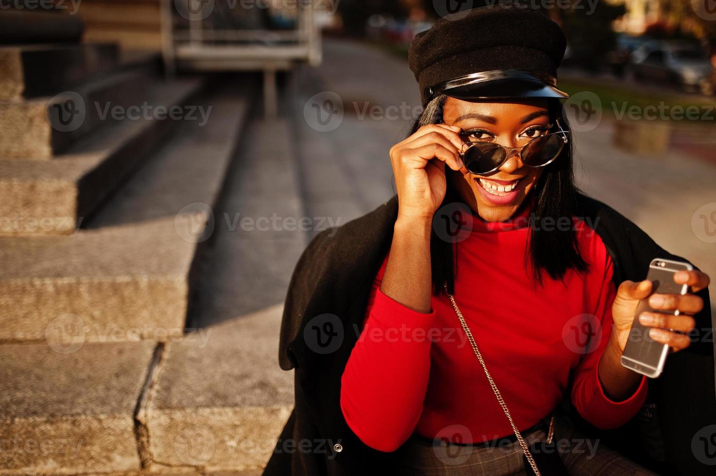 afroamerikanisches Modemädchen in Mantel und Zeitungsjungenmütze, Sonnenbrille auf der Straße gestellt. foto