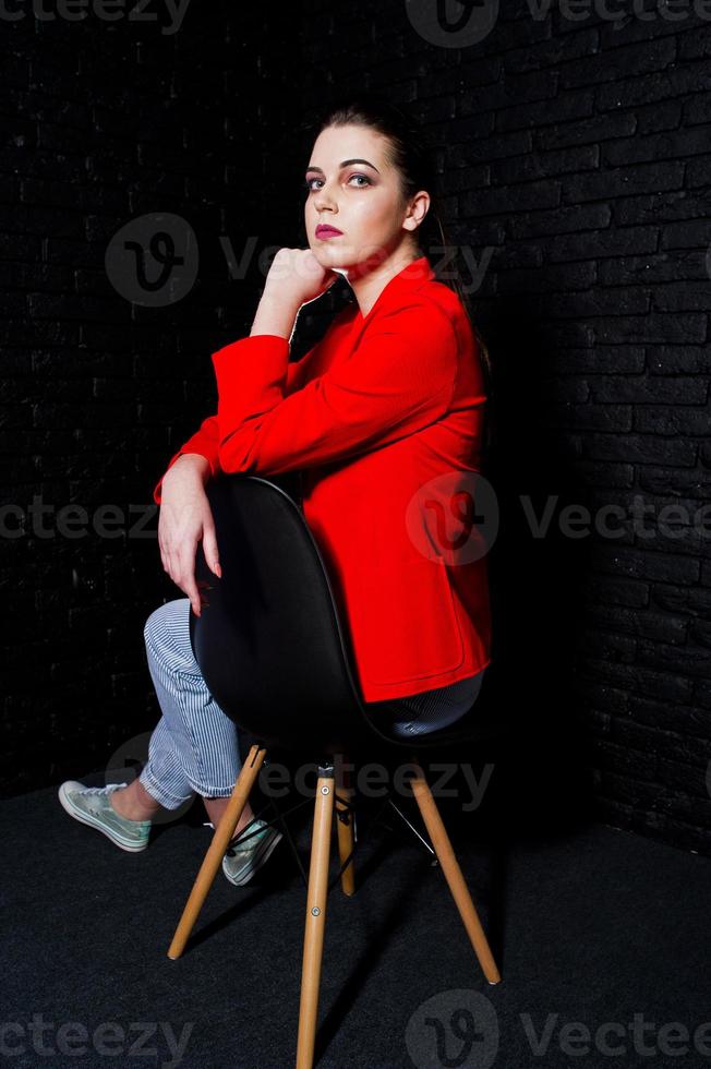 stilvolles brünettes mädchen auf roter jacke gegen studioschwarze backsteinmauer. foto