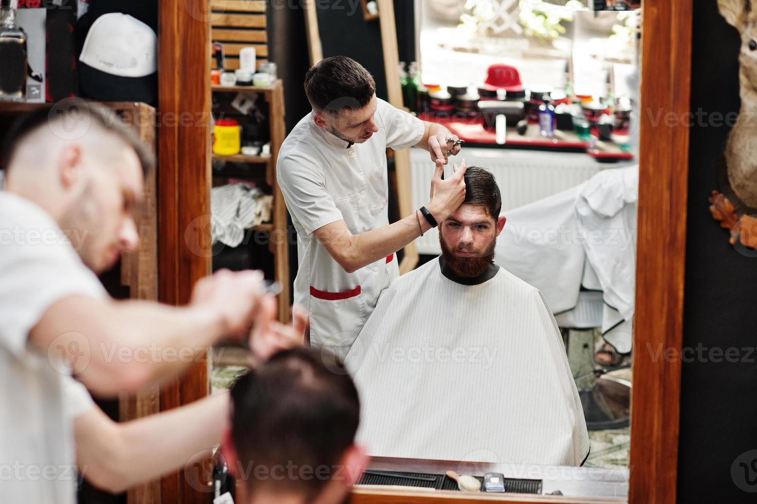 junger bärtiger mann, der vom friseur die haare schneiden lässt, während er im friseursalon auf dem stuhl sitzt. Barbier Seele. foto