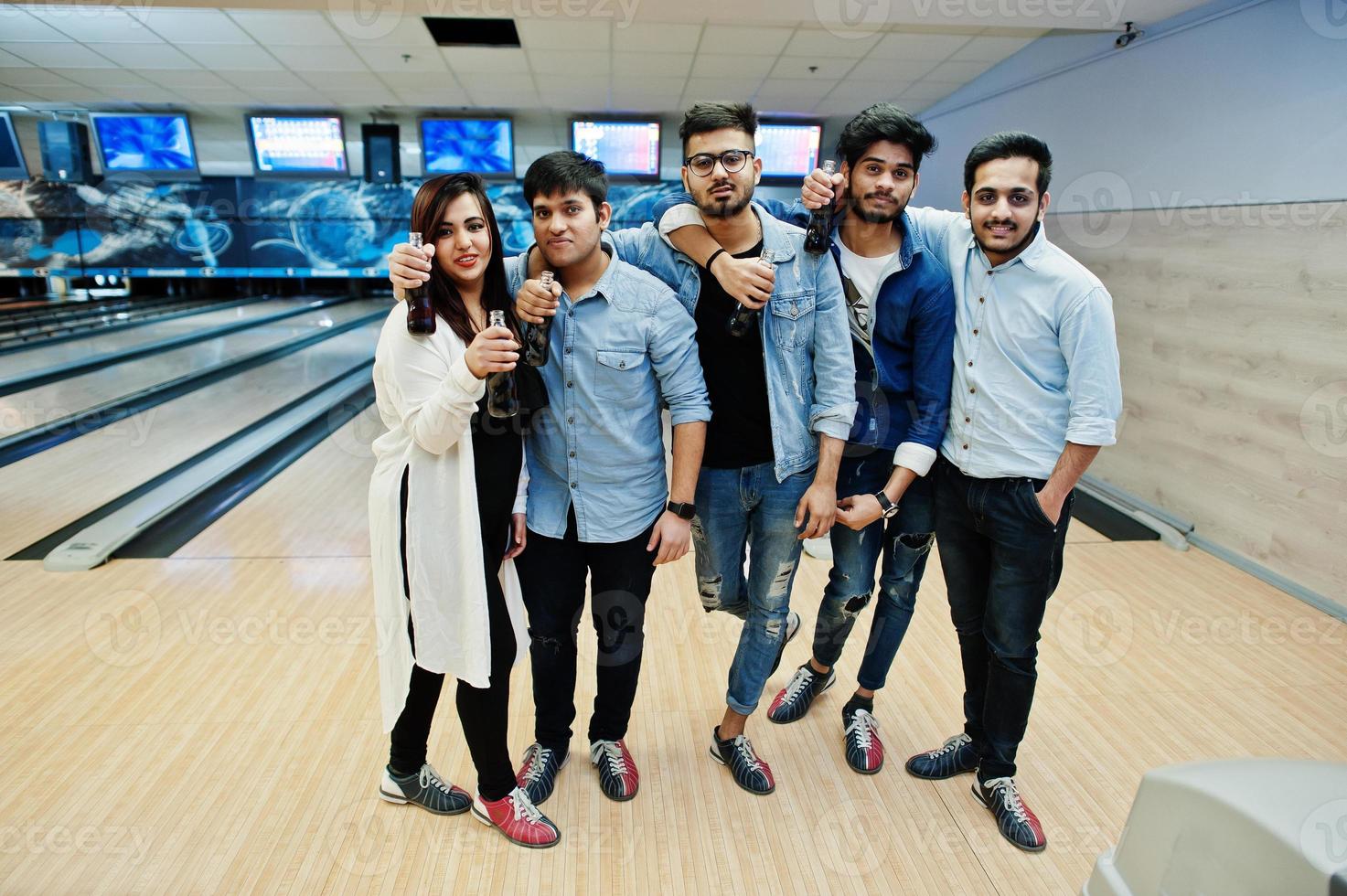 Gruppe von fünf südasiatischen Völkern, die sich im Bowlingclub ausruhen und Spaß haben. hält kalte Sodagetränke aus Glasflaschen. foto