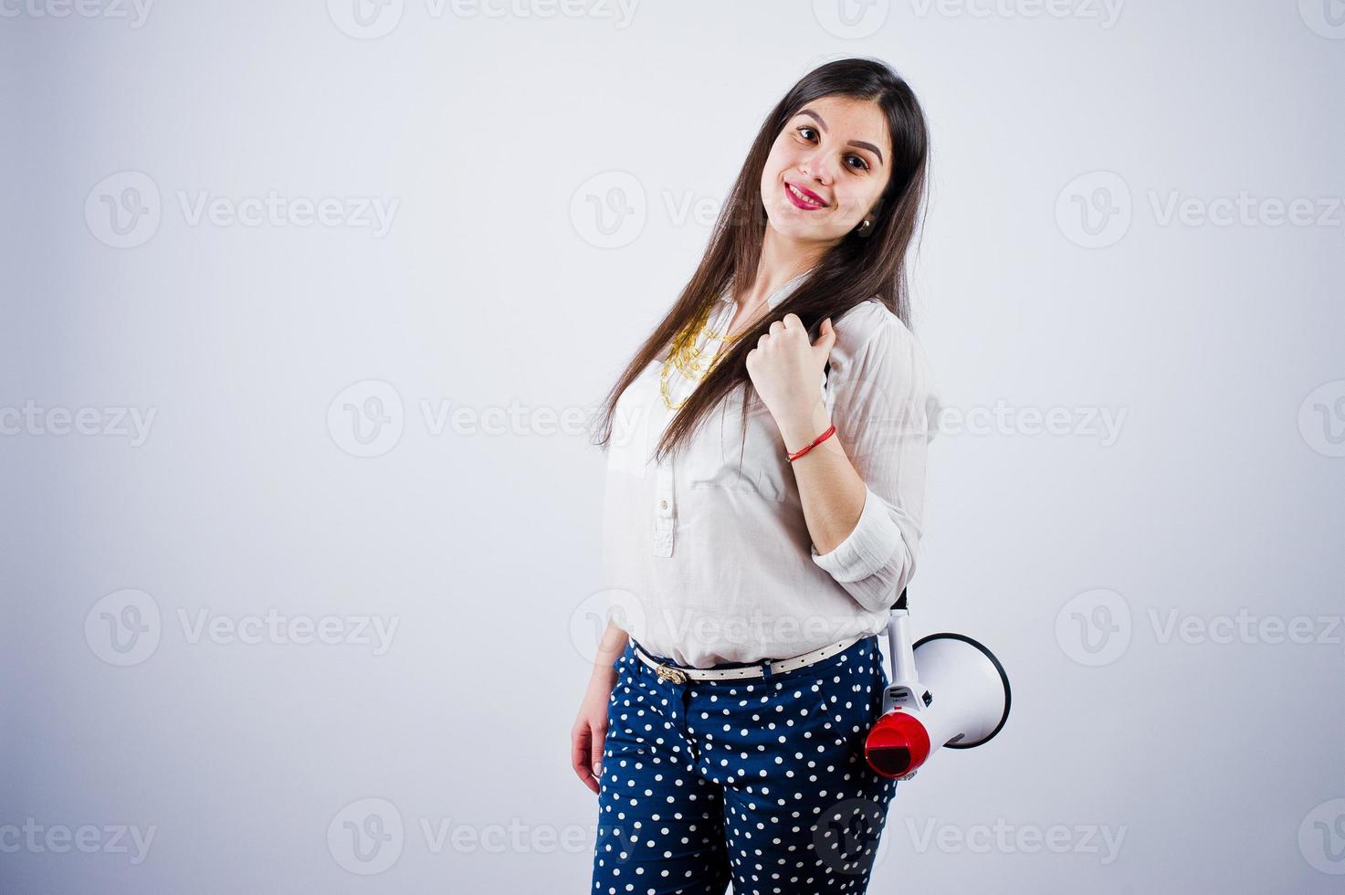 Porträt einer jungen Frau in blauer Hose und weißer Bluse, die im Studio mit Megaphon posiert. foto