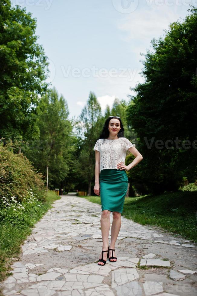 Brunettemädchen im grünen Rock und in der weißen Bluse stellte am Park auf. foto