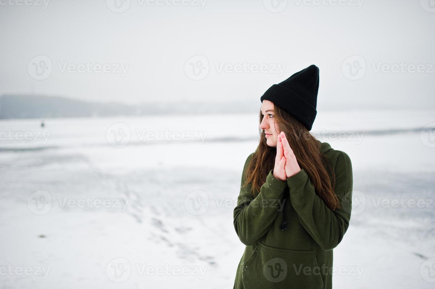 lustige mädchen tragen auf langem grünem sweatshirt, jeans und schwarzer kopfbedeckung, am zugefrorenen see am wintertag. foto