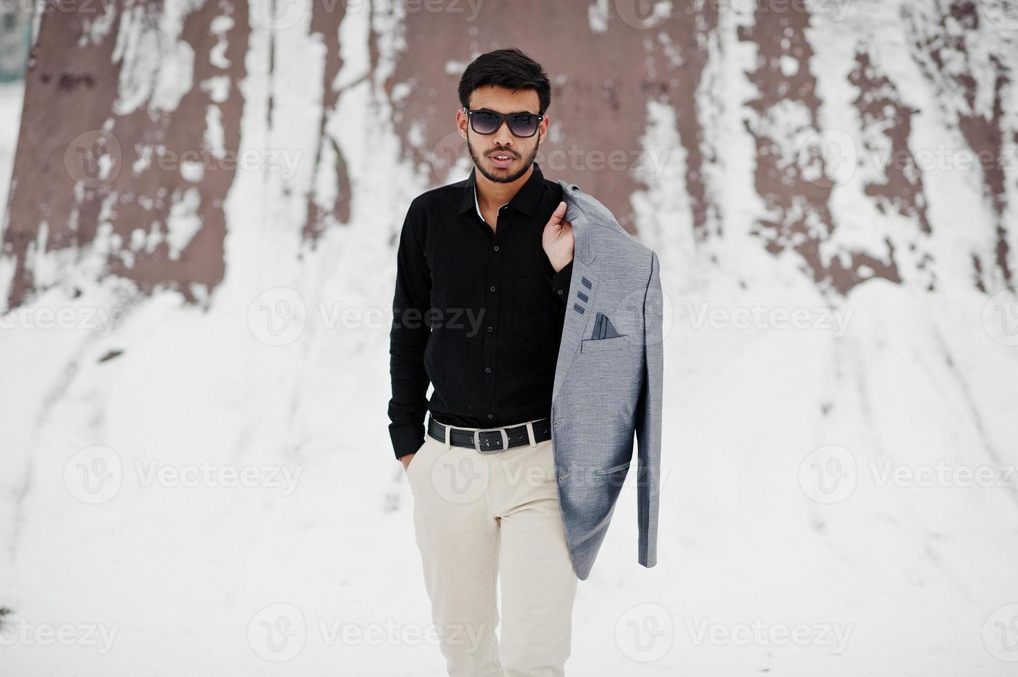 Lässiger junger indischer Mann in schwarzem Hemd und Sonnenbrille mit Jacke auf den Schultern posierte am Wintertag. foto