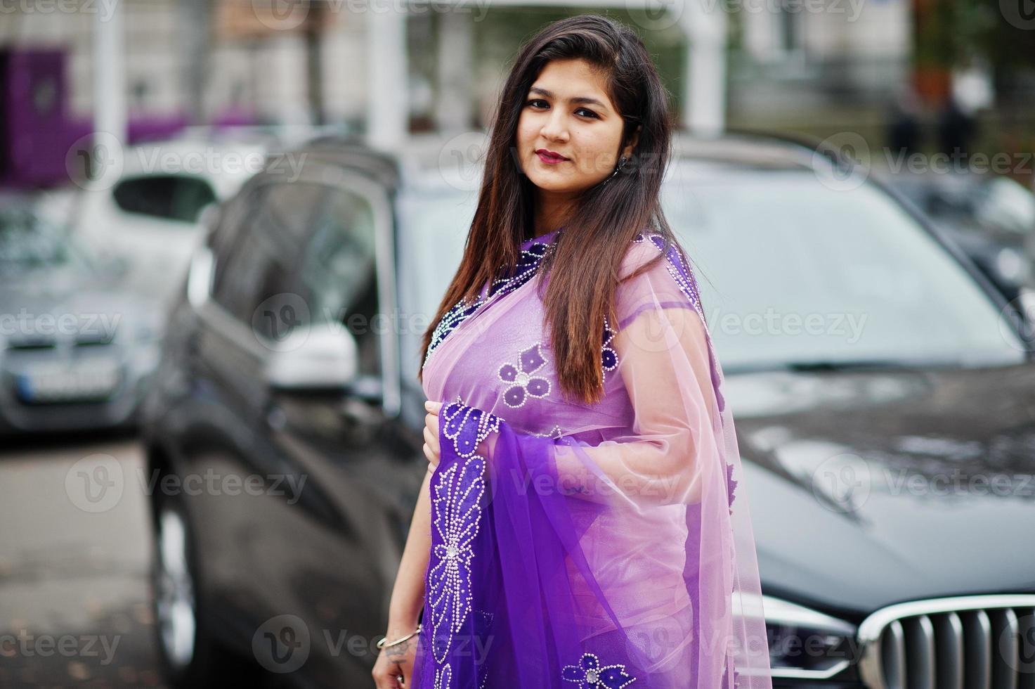 Indisches hinduistisches Mädchen im traditionellen violetten Saree posierte auf der Straße gegen schwarzes Business-SUV-Auto. foto