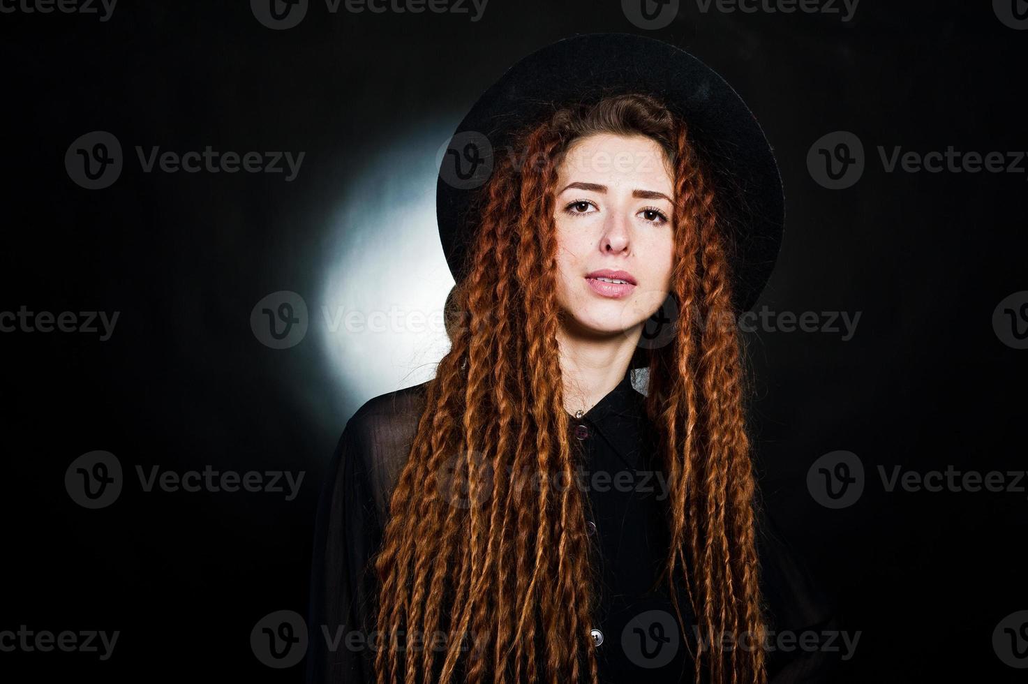 Studioaufnahme eines Mädchens in Schwarz mit Dreadlocks und Hut auf schwarzem Hintergrund. foto