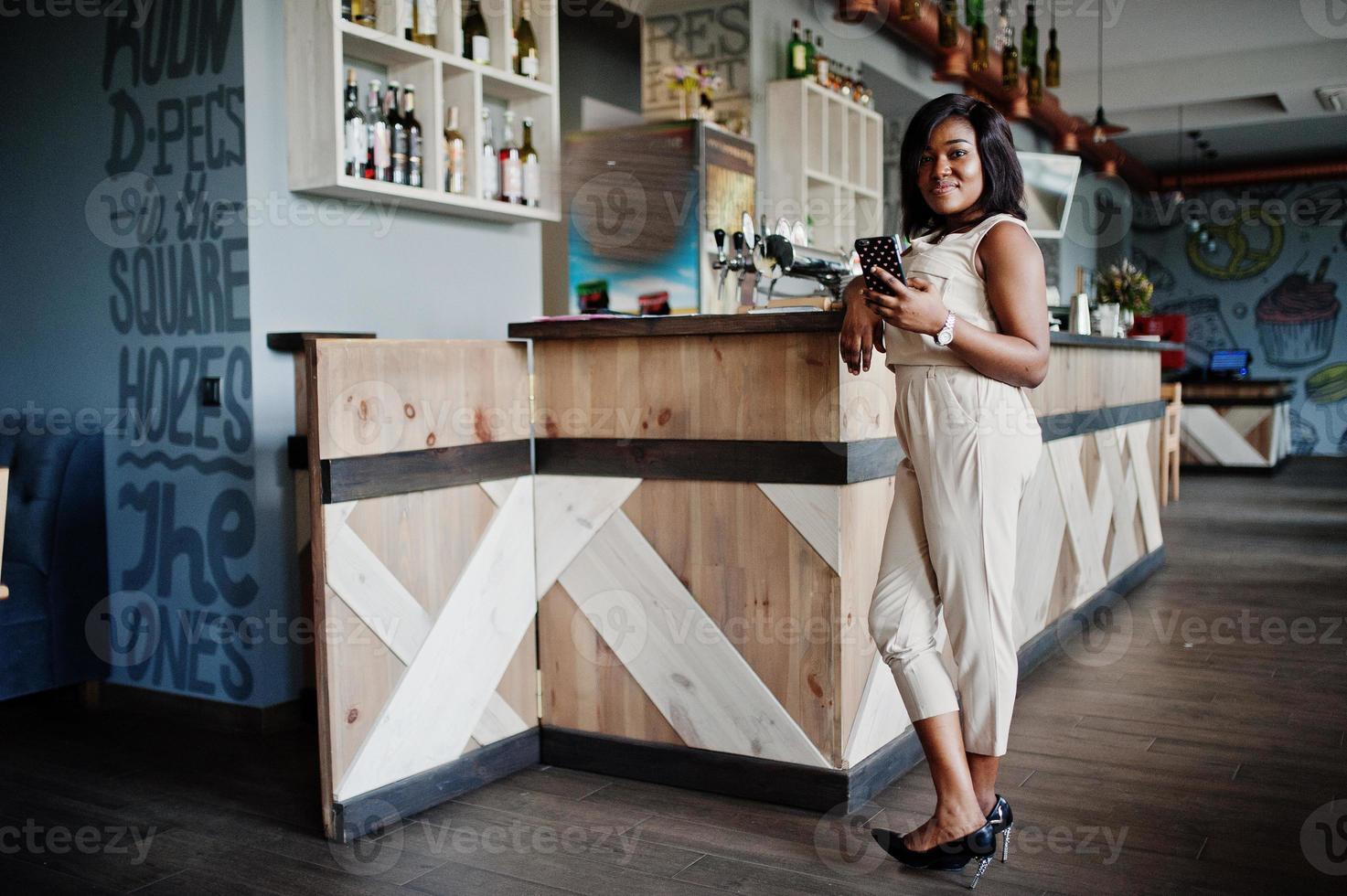 Afroamerikanisches Mädchen posierte im Café mit Handy zur Hand. foto